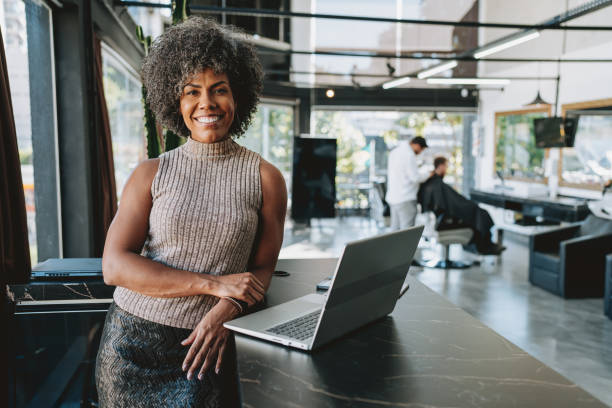 Smiling business owner in a modern salon with a laptop, showcasing efficient business management and cost-saving strategies on commercial electricity plans.